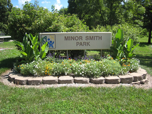 minor smith sign surrounded by white, yellow and red flowers and large plants