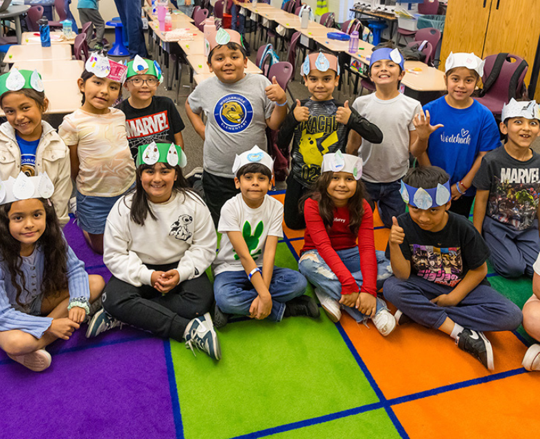 Elementary class sitting on colorful rug wearing water crowns